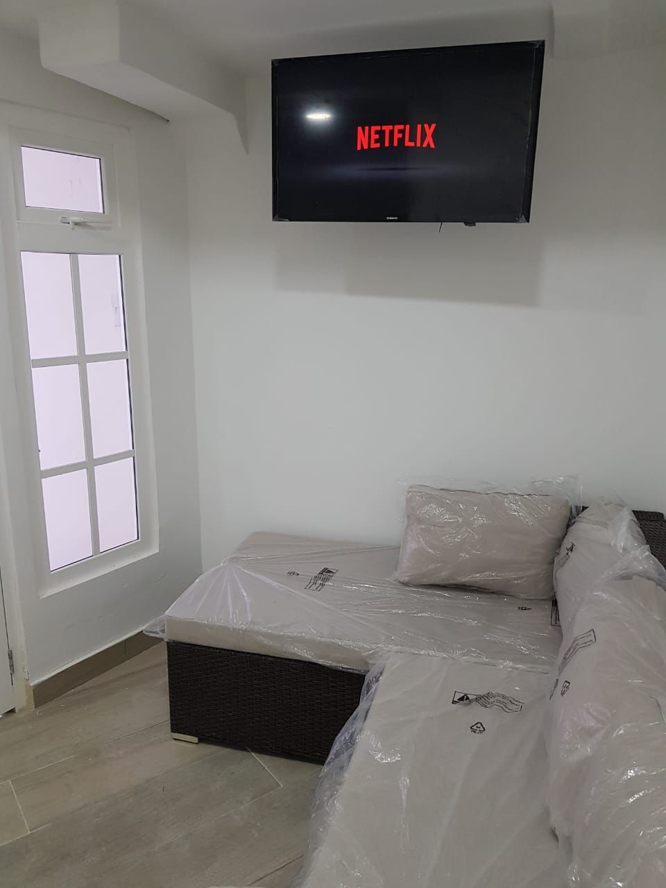 A room with a bed, a television mounted on the wall, and a window.