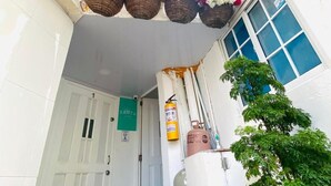 A narrow alleyway with white buildings, a green sign on a door, and a fire extinguisher.