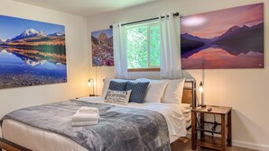 A bedroom with a bed, a window with curtains, a nightstand, and wall art depicting landscapes. - Modern Cabin - 12 Minutes to Glacier! (Hungry Horse)