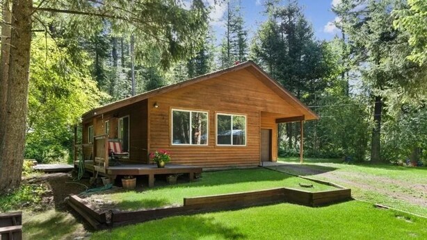 A wooden cabin with a porch, a small deck, and a well-maintained lawn. - Modern Cabin - 12 Minutes to Glacier! (Hungry Horse)