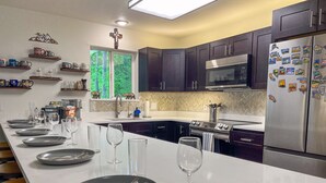 A modern kitchen with dark cabinets, stainless steel appliances, and a long island with plates and wine glasses. - Modern Cabin - 12 Minutes to Glacier! (Hungry Horse)
