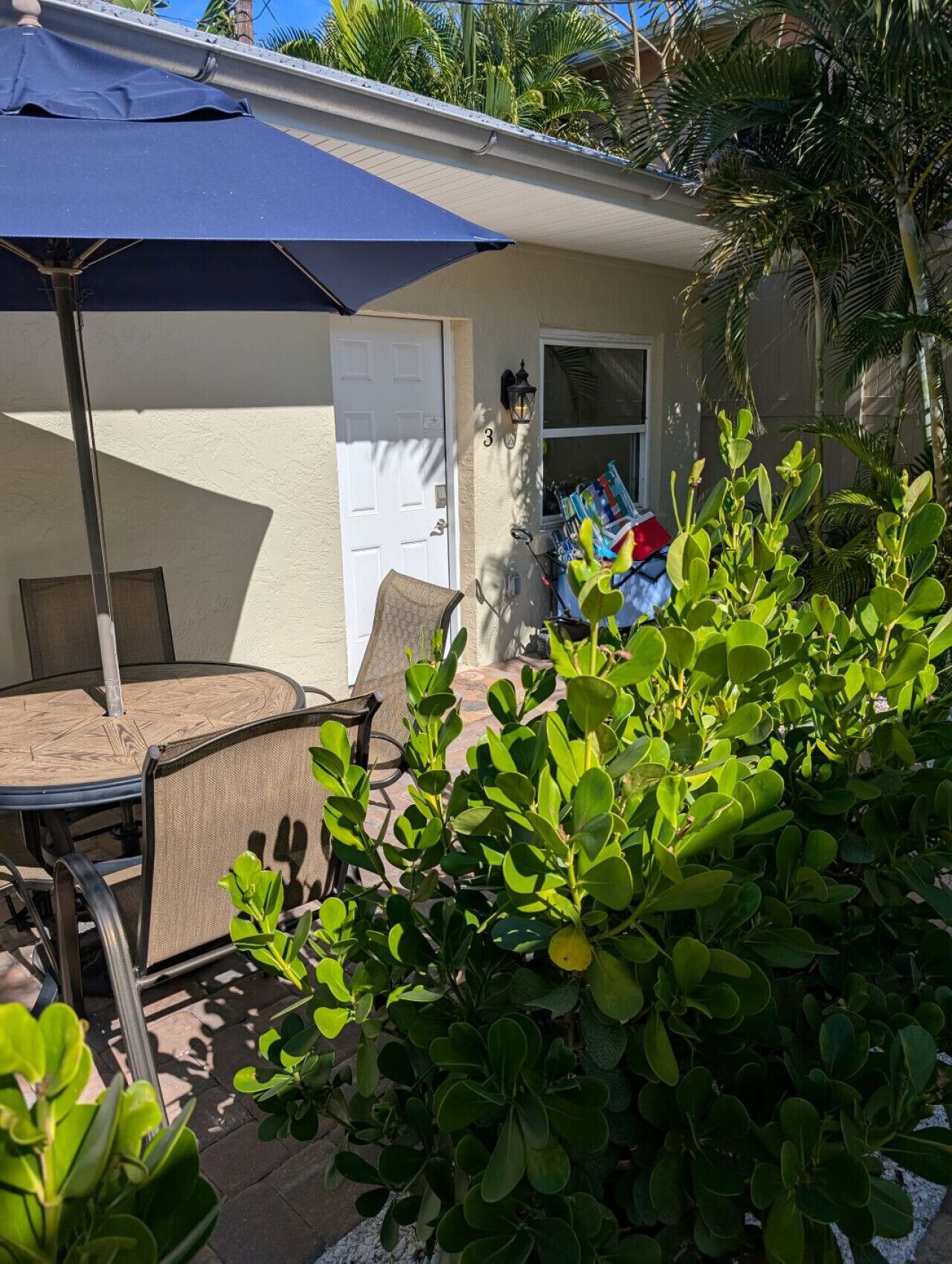 A patio area with a table and chairs, a blue umbrella, and a door.