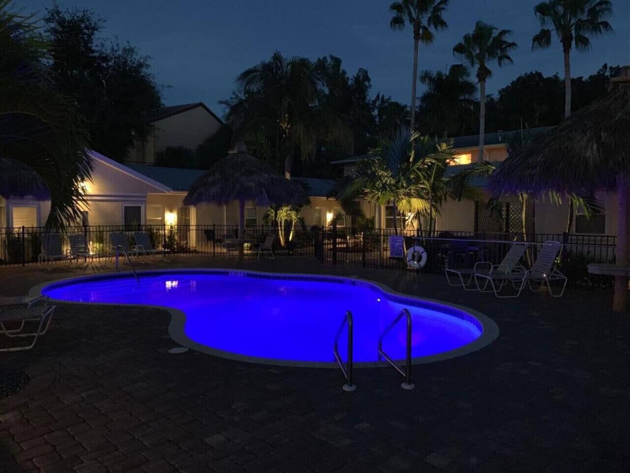 A swimming pool at dusk with lounge chairs and a fence.