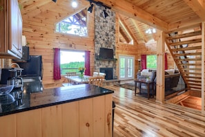 A log cabin with a stone fireplace, wooden floors, and a kitchen area.