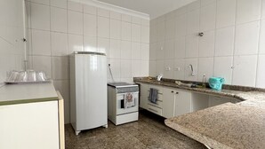 A kitchen with white cabinets, a white refrigerator, a stove, and a granite countertop. - Grande Familia Hostel (São Paulo)