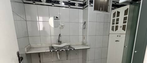A bathroom with white tiles, a sink, a toilet, and a shower area.