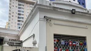 A hostel with a white facade, a large window displaying multiple flags, and a door with a sign above it. - Grande Familia Hostel (São Paulo)