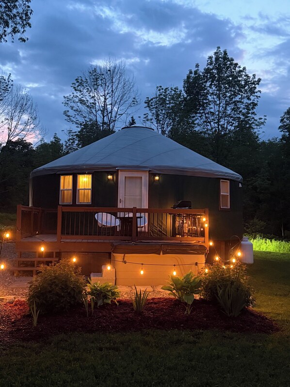 A single-story, A-frame structure with a porch and a covered deck area, surrounded by a landscaped garden.