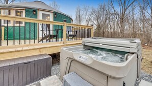 A yurt with a wooden deck and a hot tub.