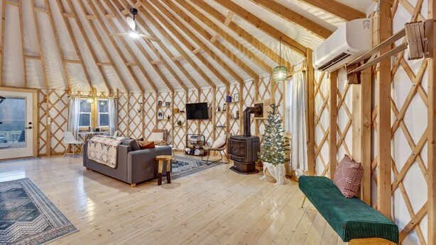A spacious, naturally lit interior with a high wooden ceiling, a cozy seating area with a sofa and bench, a small table, and a decorative tree.