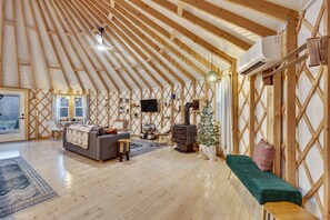 A spacious, naturally lit interior with a high wooden ceiling, a cozy seating area with a sofa and bench, a small table, and a decorative tree.