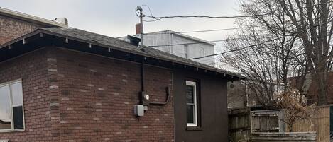 Une maison en briques avec un petit garage attenant, une allée en béton et une pelouse recouverte de feuilles.