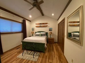 Ein Schlafzimmer mit einem Bett, einem Deckenventilator, einem Fenster mit Jalousien, einem Spiegel und einer Wand mit Dekoration.