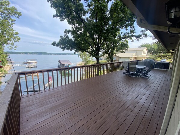 Een houten terras met uitzicht op een meer, een steiger en een overdekte barbecueplek.