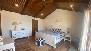 Une chambre avec un plafond en bois, un lit avec une literie à rayures, une commode, une chaise et une petite table.