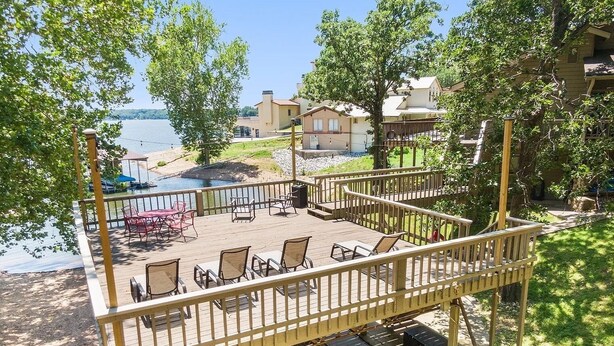 Une terrasse avec des sièges extérieurs donnant sur un lac, entourée d’arbres et d’un bâtiment.