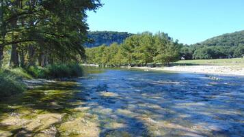 Un río de aguas cristalinas, rodeado de árboles y un área cubierta de pasto.