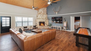 A spacious living room with a stone fireplace, leather sofa, and a pool table. - Adelante · Outdoor Theater~Near River~Pool~Hot Tub~Mini Golf (Concan)