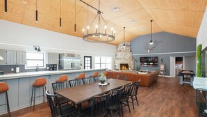A spacious kitchen with a long island, a dining area with a wooden table, and a stone fireplace. - Adelante · Outdoor Theater~Near River~Pool~Hot Tub~Mini Golf (Concan)