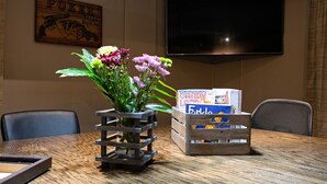 Una mesa de madera con un centro de mesa floral, un televisor montado en la pared y un baúl de madera con cajas de dulces.