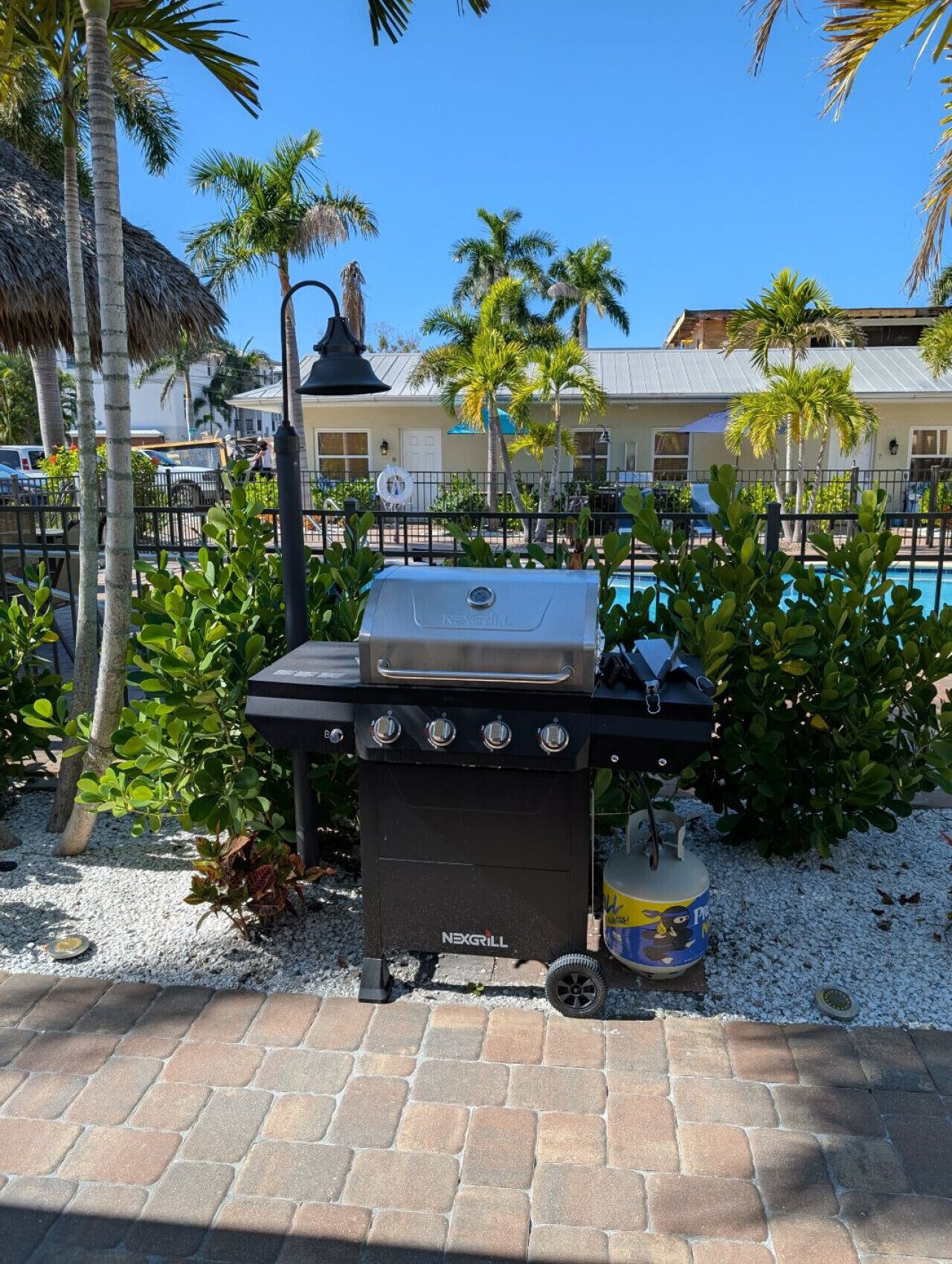 En sort NexGrill barbecue med fire brændere, en propanflaske og en sort lanterne.