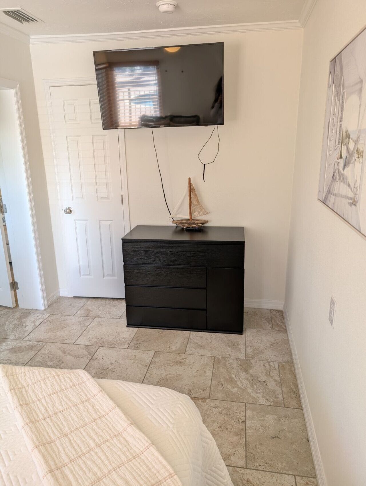 Une chambre à coucher avec un lit, une commode, un téléviseur fixé au mur et une porte.
