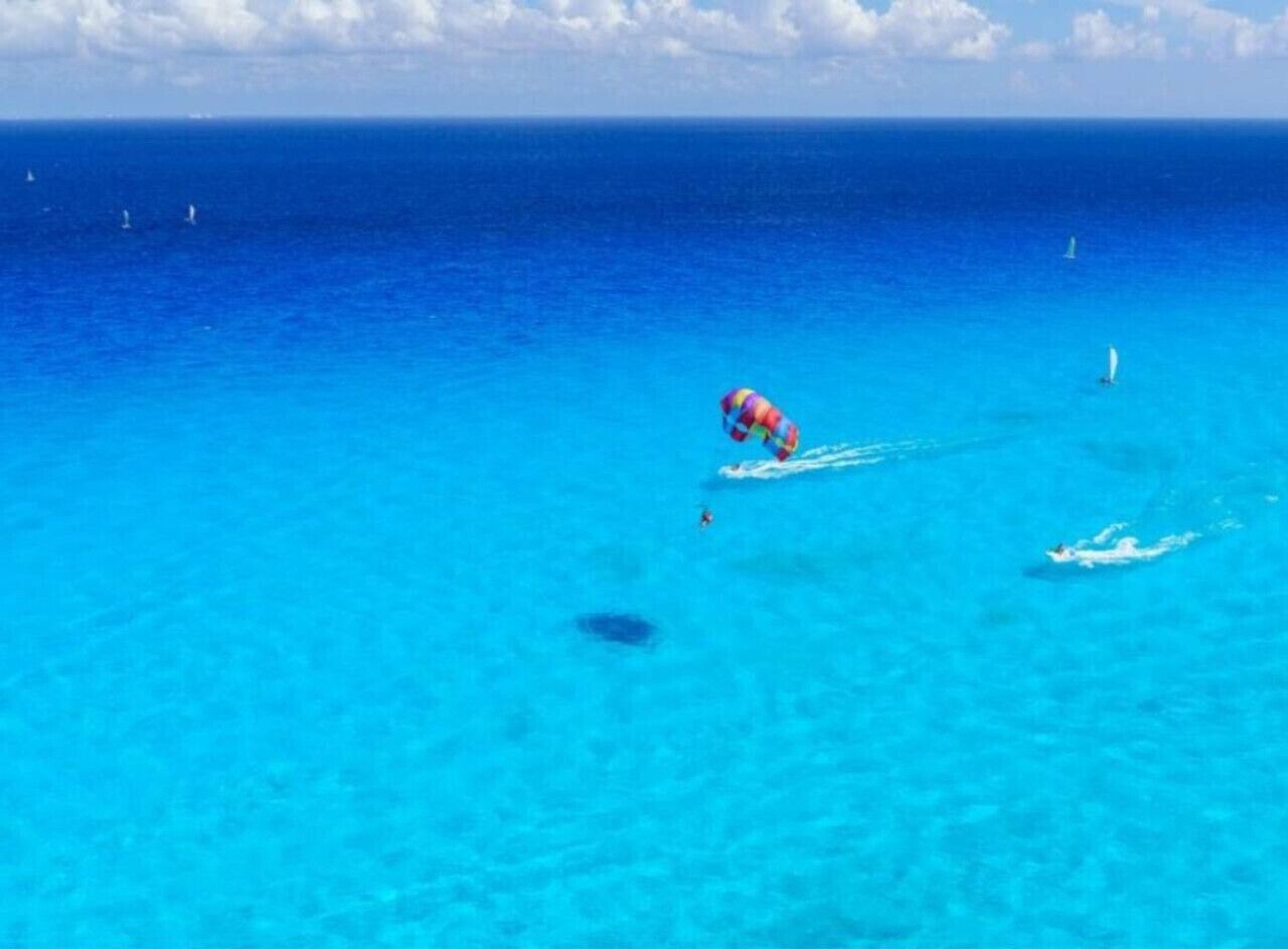 En tydlig bild av en strand med en person i en färgglad badklädesdräkt som simmar i vattnet.