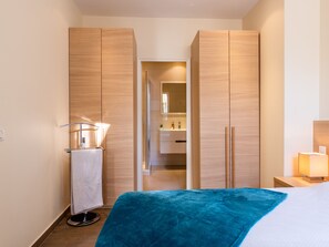 Habitació d'hotel amb un llit, una taula de nit, una làmpada, un bany amb mirall i armaris de fusta.