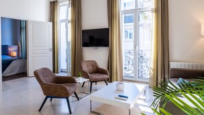 A modern hotel room with a balcony, a flat-screen TV, two armchairs, a coffee table, and a bed with a blue headboard. - 2-Br. steps from the Palais des Festivals (Cannes)