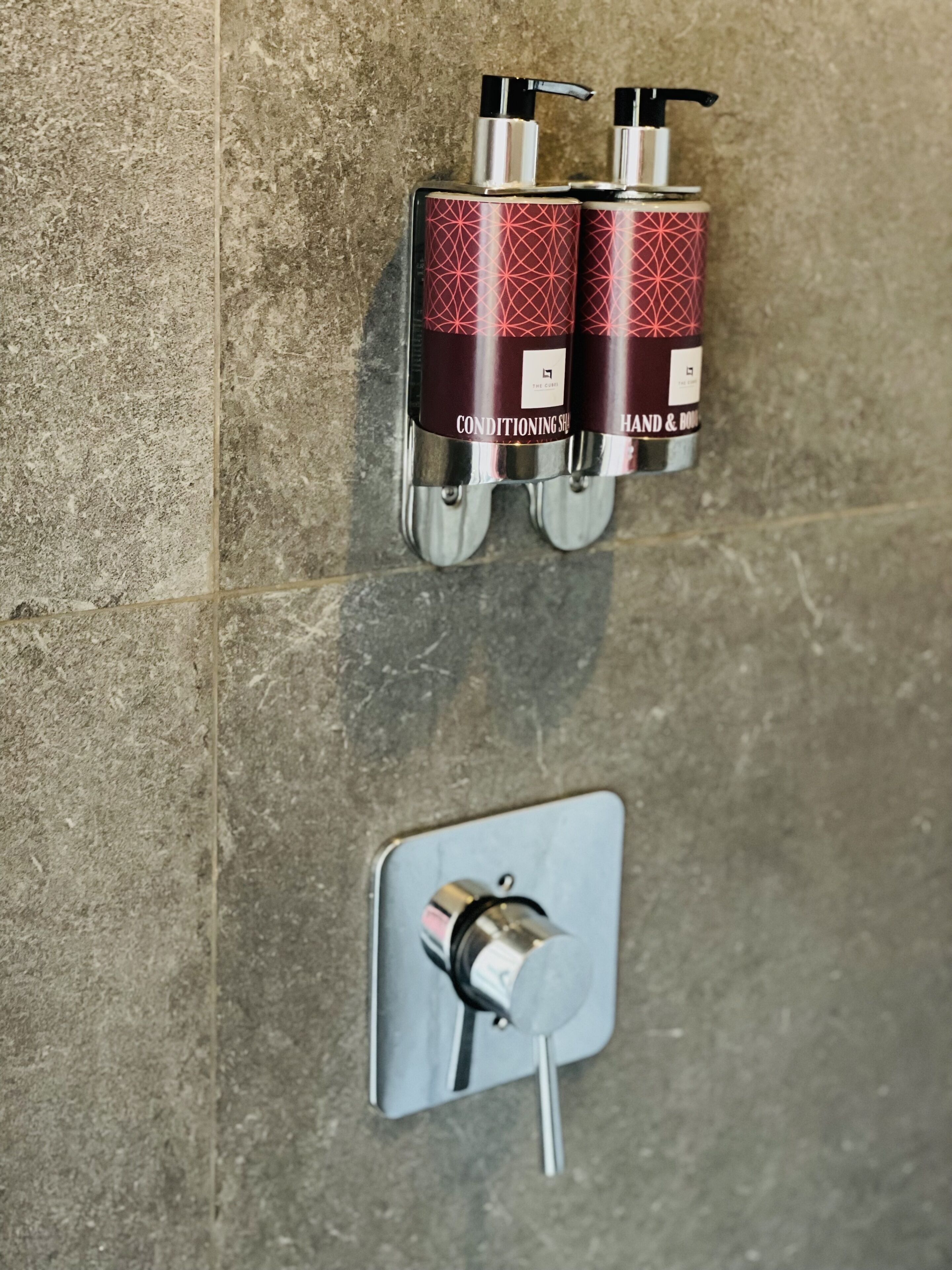 Two hand and body wash dispensers mounted on a textured wall.