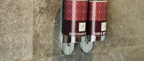 Two hand and body wash dispensers mounted on a textured wall.