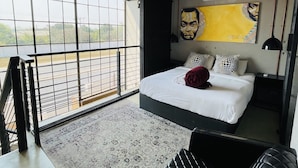 A modern bedroom with a large bed, a view through floor-to-ceiling windows, and a unique artwork on the wall. - The Cubes Apartments (Lusaka)