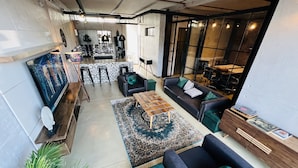 A modern living room with a sofa, coffee table, and a patterned rug. There are bar stools and a bar area in the background. - The Cubes Apartments (Lusaka)