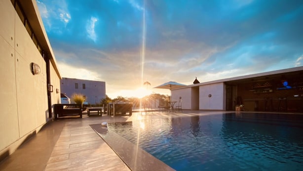 A swimming pool with a wooden deck, a bar area, and a building with a flat facade. - The Cubes Apartments (Lusaka)