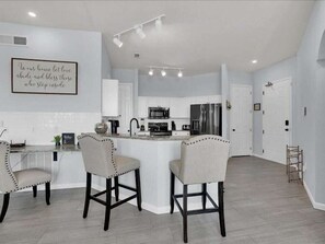Una cocina moderna con una isla central, taburetes de bar y una pared destacada con una cita inspiradora.