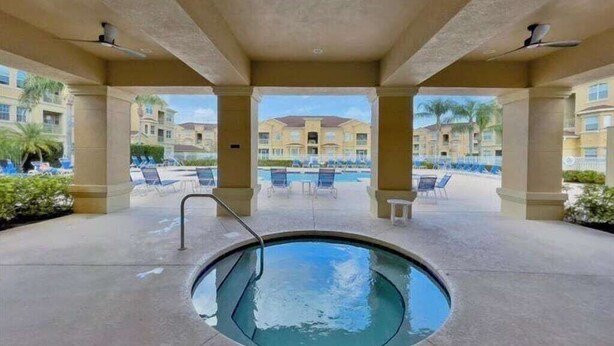Ein runder Whirlpool in einer überdachten Außenbereich mit Liegestühlen und einem Pool im Hintergrund.