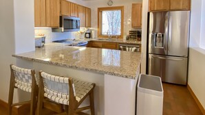 Eine moderne Küche mit Granit-Arbeitsplatten, Holzschränken, Edelstahlgeräten und einer Kochinsel mit Barhocker.