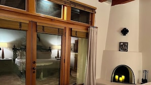 Ein Zimmer mit einer großen Schiebeglastür, die auf einen Balkon führt, einem Kamin mit drei Kerzen und einer Bank neben der Tür.