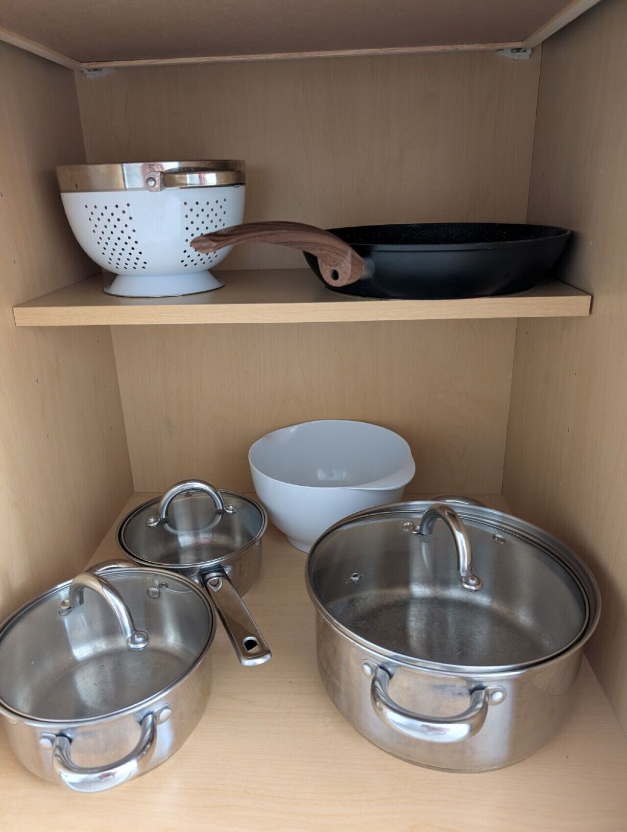 A kitchen shelf with various cookware including a colander, a frying pan, and several pots.