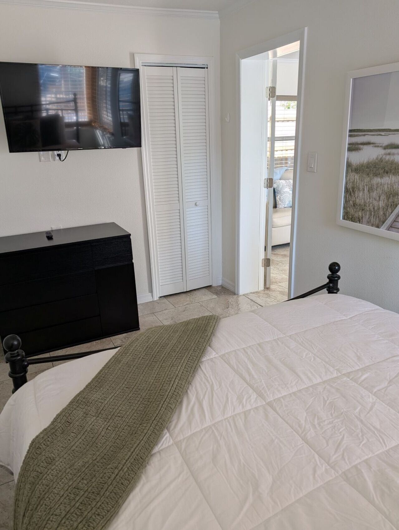 Een slaapkamer met een bed, een dressoir, een televisie, een kast en een deur die leidt naar een balkon.