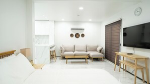 A modern bedroom with a large bed, a sofa, a TV, and a desk. - Mariana Suites (Saipan)