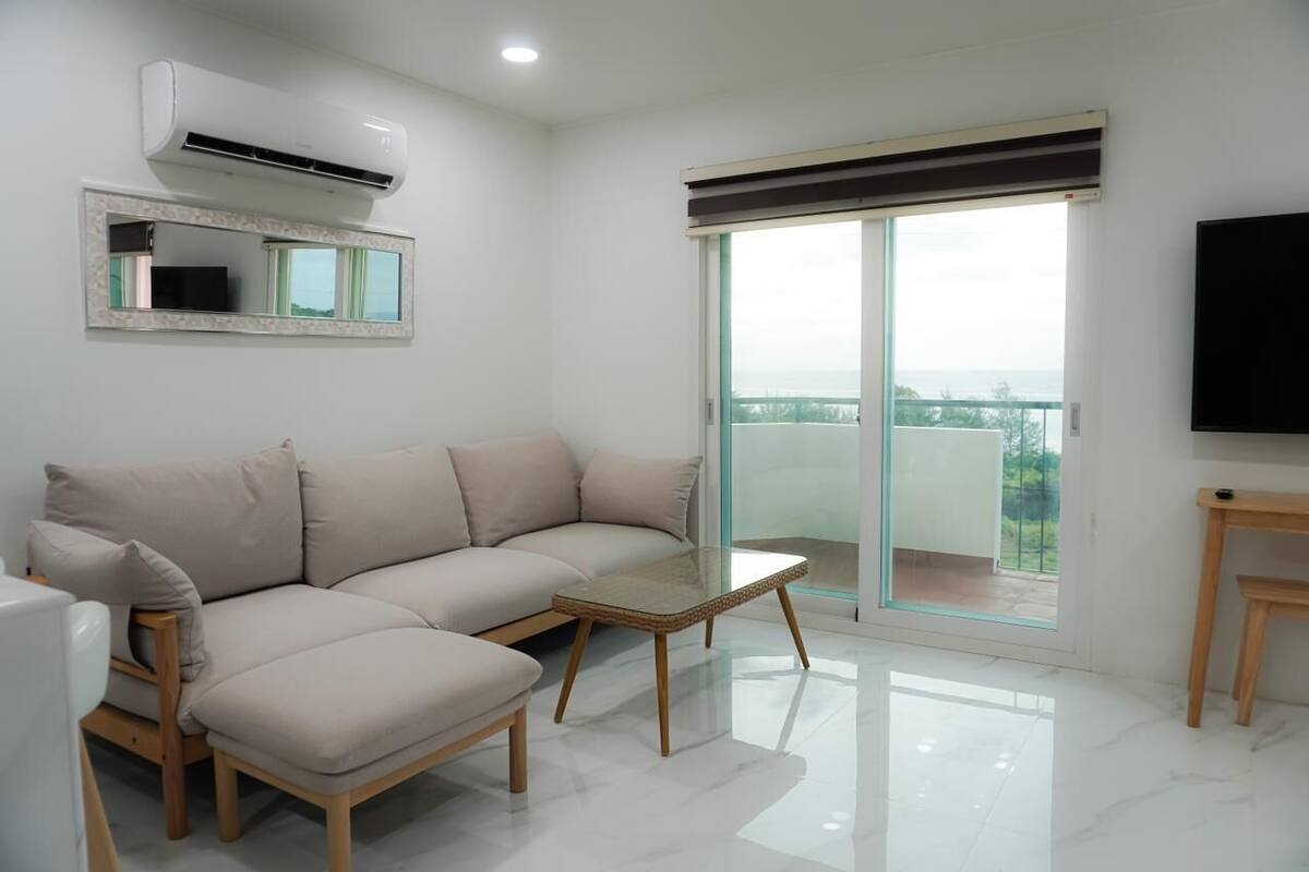 A modern living room with a beige sofa, a glass-top coffee table, and a flat-screen TV on a wooden stand.