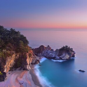 A coastal landscape with rocky cliffs, a sandy beach, and a calm sea.