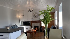 A modern living room with a fireplace, a television, and a dining area with a vase of flowers. - Cottage 433 - Ballyconneely - sleeps 2 guests  in 1 bedroom (Ballyconneely)