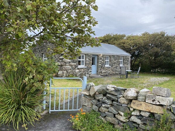 A stone house with a blue door, a stone wall, and a metal gate.
