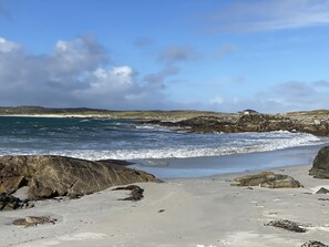 A rocky beach with waves crashing onto the shore, a sandy beach in the foreground, and a building on the right side. - Cottage 433 - Ballyconneely - sleeps 2 guests  in 1 bedroom (Ballyconneely)