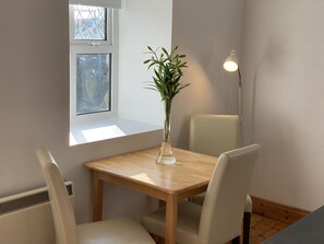 A dining area with a wooden table, two chairs, a vase with green plants, and a floor lamp. - Cottage 433 - Ballyconneely - sleeps 2 guests in 1 bedroom (Ballyconneely)