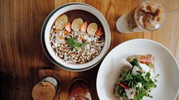 A dining table with a bowl of oatmeal topped with fruits and nuts, a glass of iced coffee, and a plate of salad.
