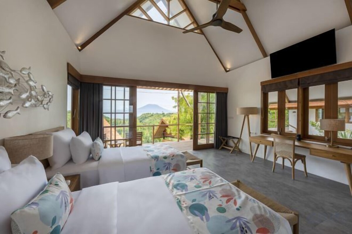 A spacious bedroom with two beds, a desk, and a chair, with a large window offering a view of the outdoors.