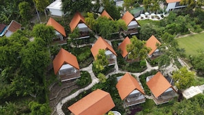 Vista aérea de un resort con varias cabañas de estilo bungalow, cada una con techo inclinado, rodeadas de abundante vegetación y un paisaje bien cuidado.